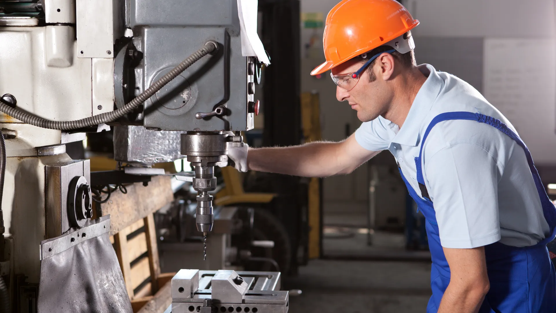 Machine operator drilling a precision metal component on an industrial drill press